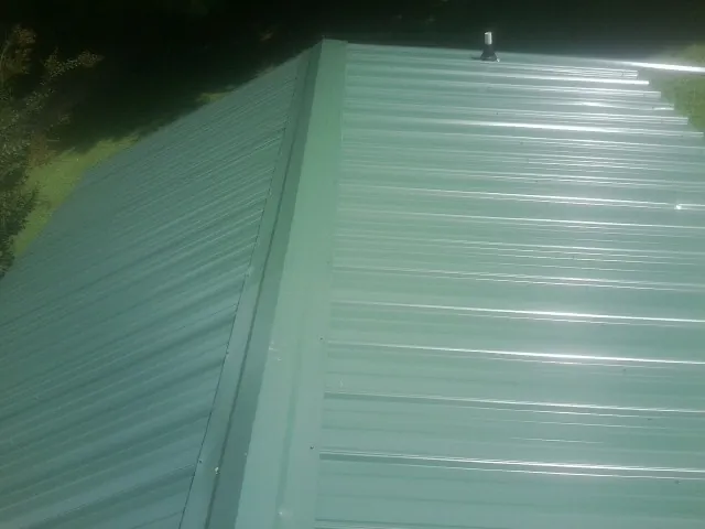 New green metal panels meeting at the ridge of a roof — Flat Roof Repair work by our crew in Naples